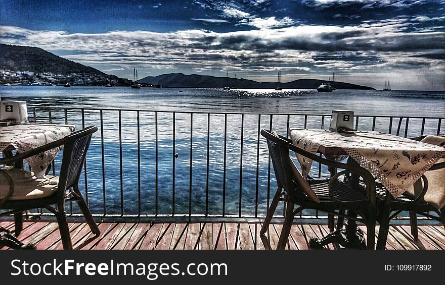 White Table With Two Armchair Set Near Body of Water and Mountain