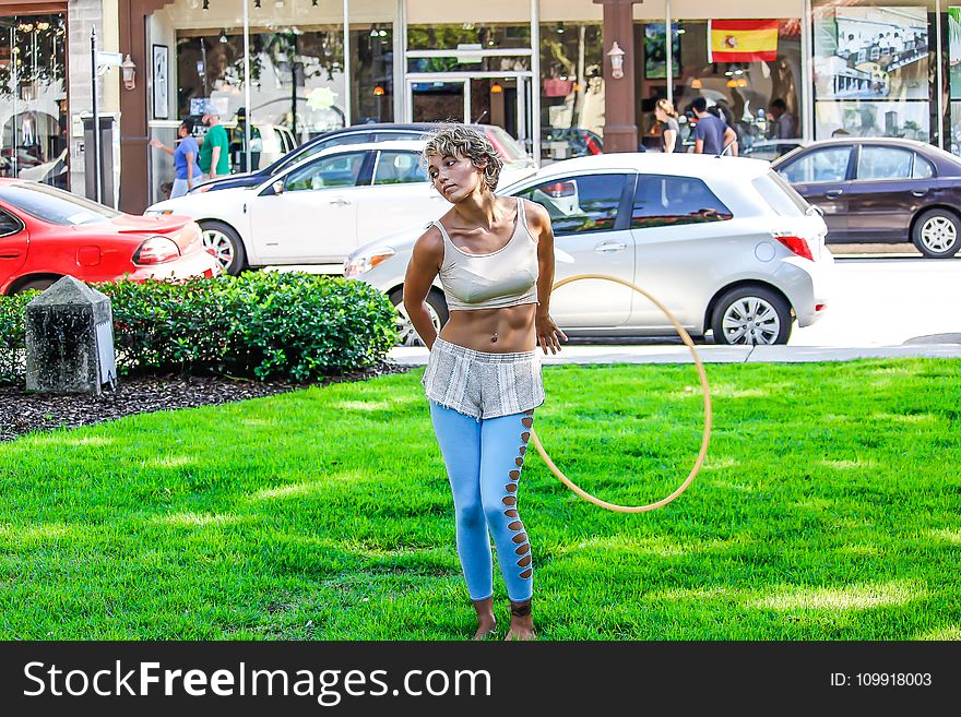 Woman in White Sleeveless Shirt and Blue Pants Holds Yellow Hula Hoop Stands on Green Grass