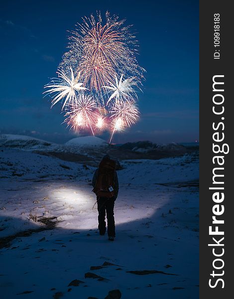 Person Stands on Snow Covered Mountain Looking at Fireworks