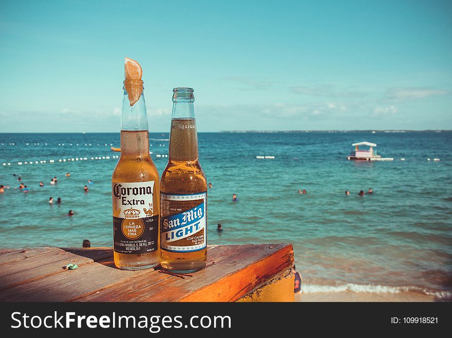 Two Corona Extra And San Mig Light Beers On Top Of Brown Wooden Plank Near Beach