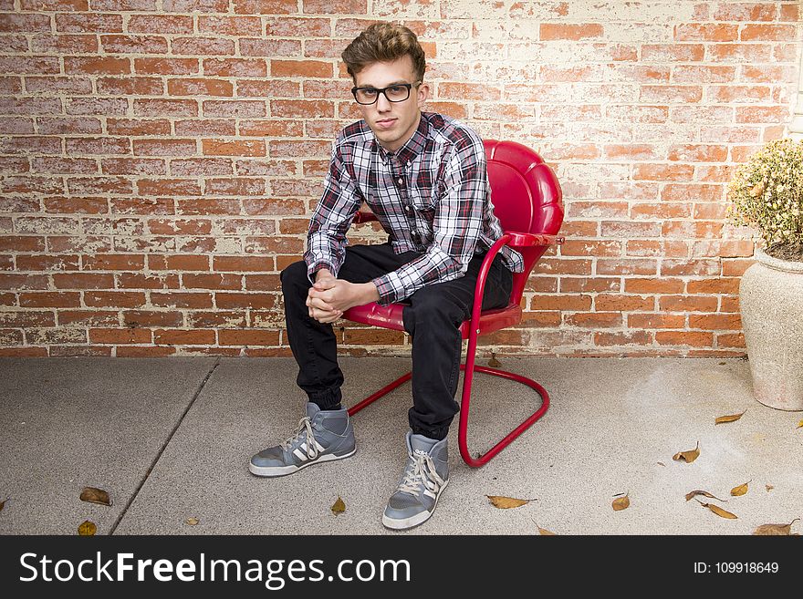 Man In Plaid Long-Sleeved Shirt And Black Pants Sitting On Red Chair