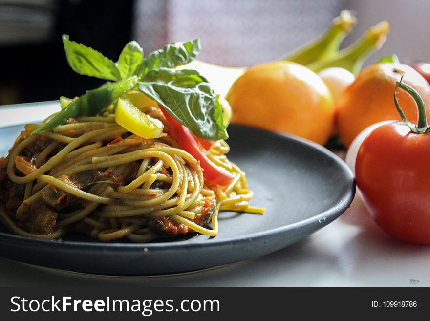 Pasta With Vegetable Dish on Gray Plate Beside Tomato Fruit on White Table