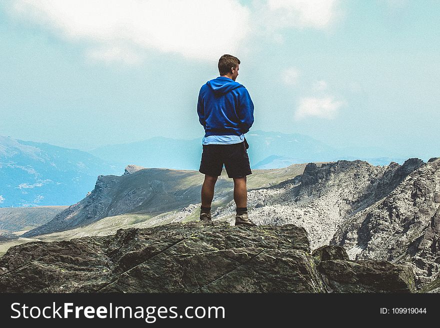 Man Wearing Blue Hoodie Standing on Top of Mountain