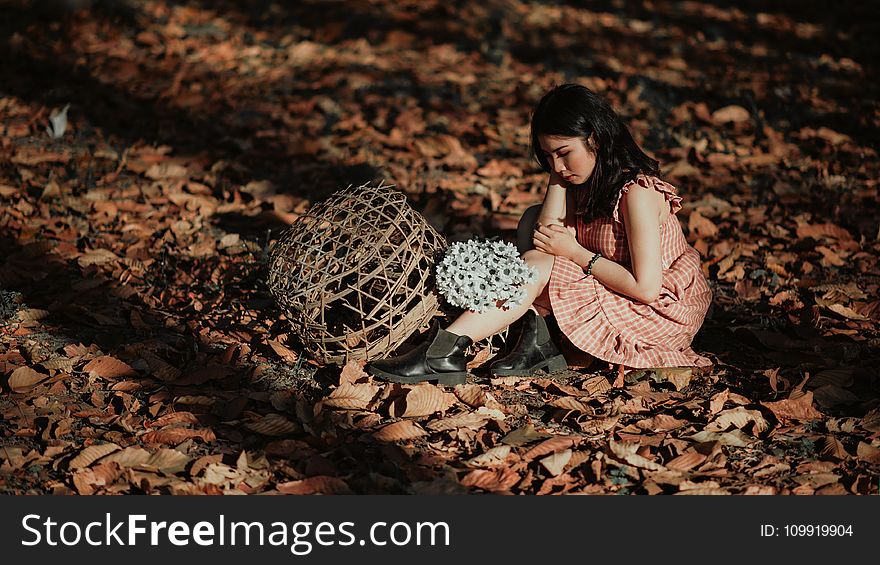 Woman Wearing Red Dress Sitting On Brown Ground With Woven Brown Basket