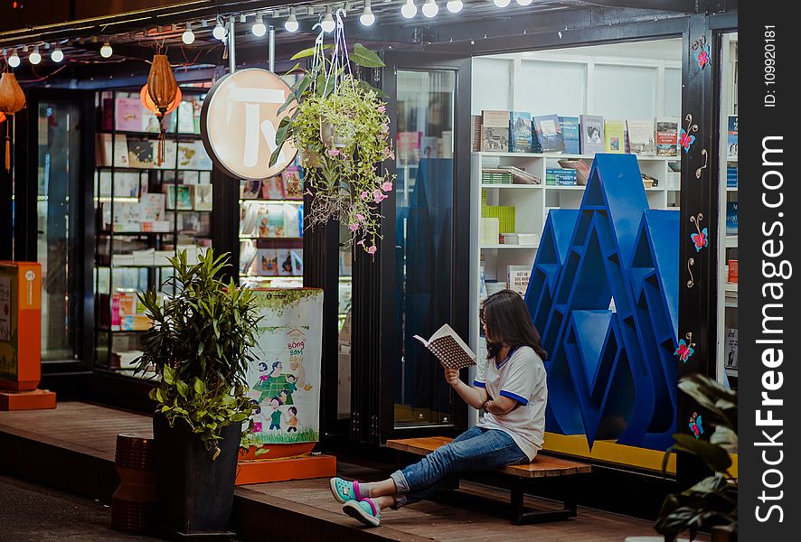 Woman Sitting Down On Bench And Reading Infront of Store