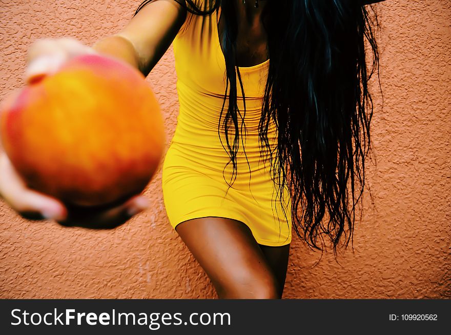 Woman Holding Round Fruit While Leaning on Orange Wall