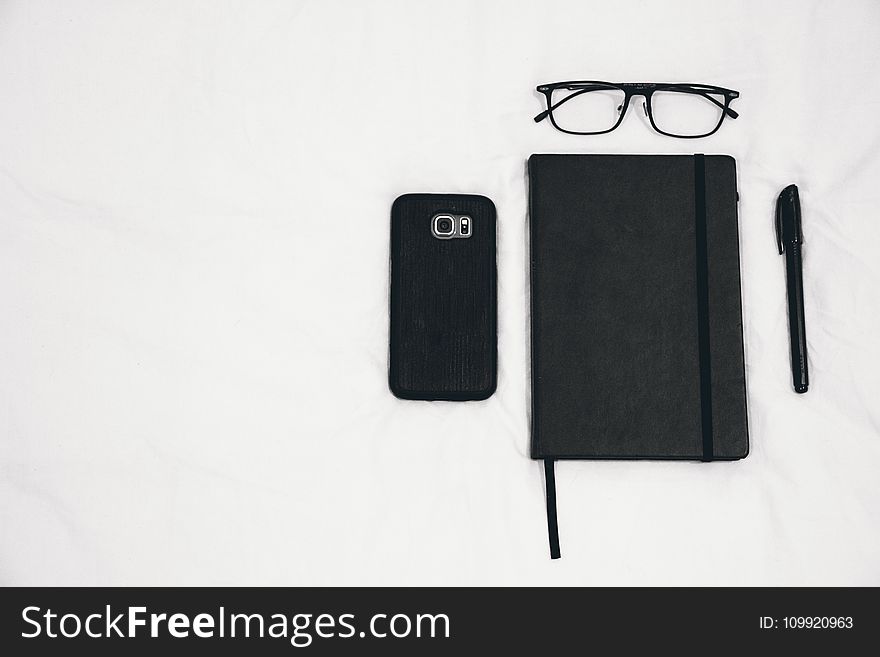 Black Smartphone Beside Planner and Eyeglasses and Pen