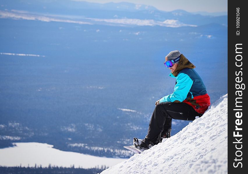 Person Wearing Blue and Red Winter Jacket Sitting on White Snow Mountain