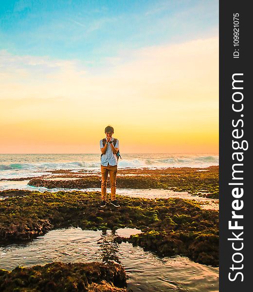 Man Standing On Rocks Near Beach During Golden Hour