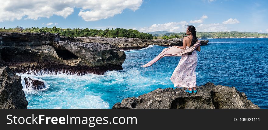 Photography of Woman Standing on Rock in Front of Sea