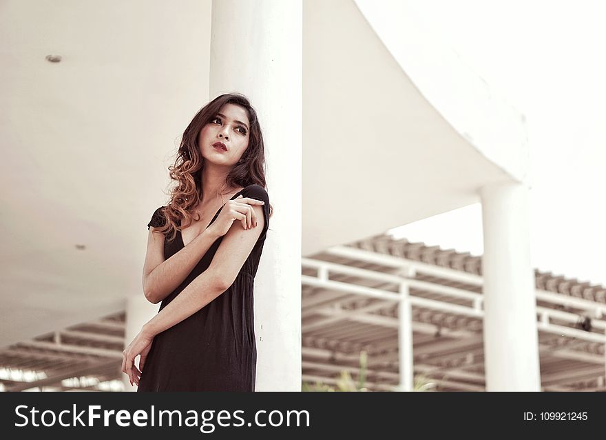 Woman in Black Plunging Neck Dress Standing Behind White Concrete Pillar