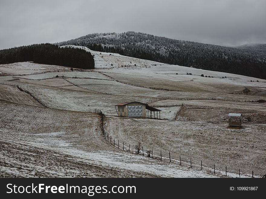 Brown Wooden House Surrounded With Brown Field Near Mountain Under Gray Sky at Daytime