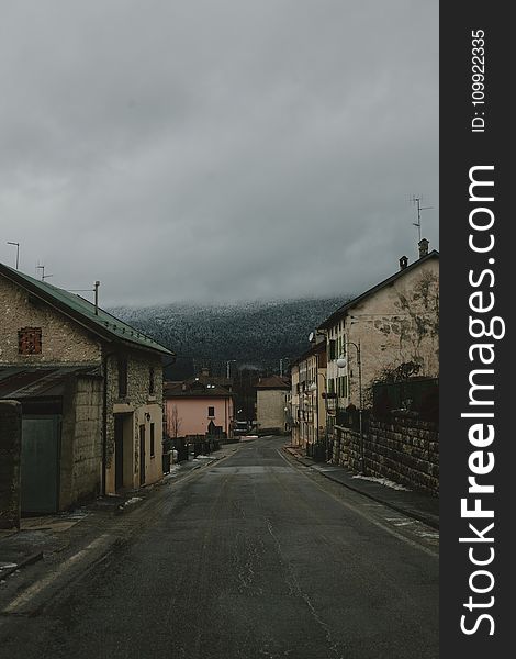 Gray Road Surrounded With Concrete Houses With Background of Dark Clouds