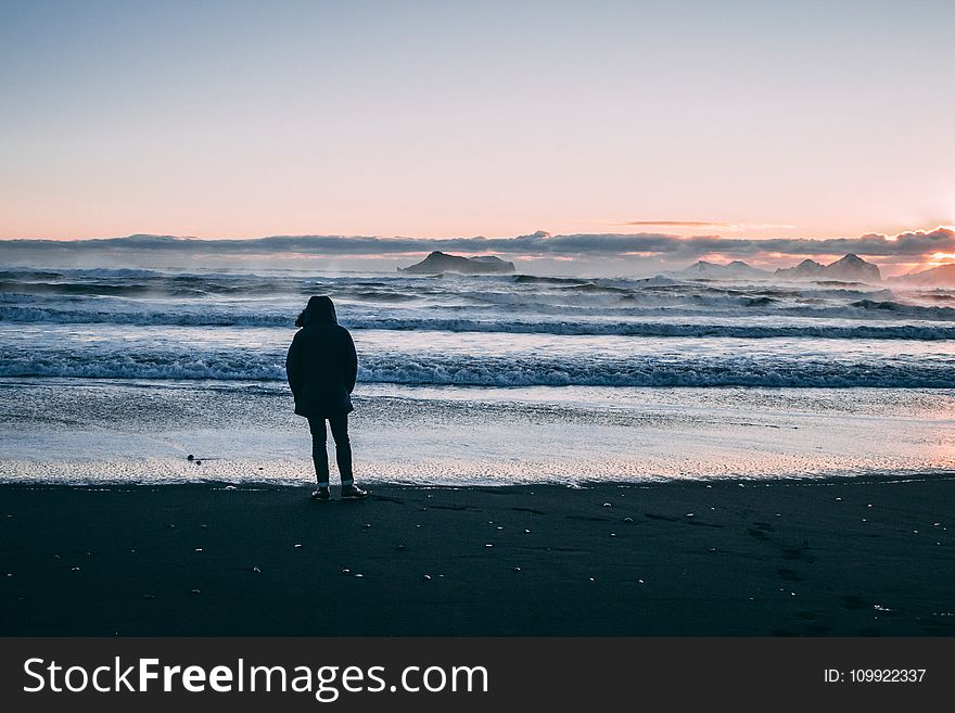 Person Standing on Beach Seashore during Sunset