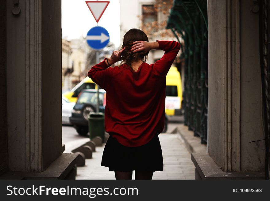 Woman in Red Sweater and Black Miniskirt Holding Hair Facing Road