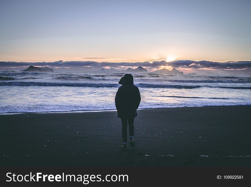 Person in Black Hoodie Near Seashore during Sunset