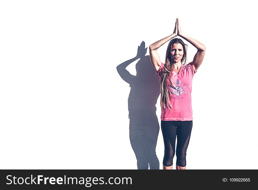 Woman in Pink Crew-neck T-shirt and Black Leggings Standing Near White Wall