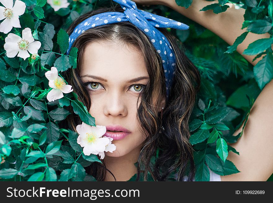 Portrait Photo of Woman in White Top and Blue Polka Dot Headband Near Flowers