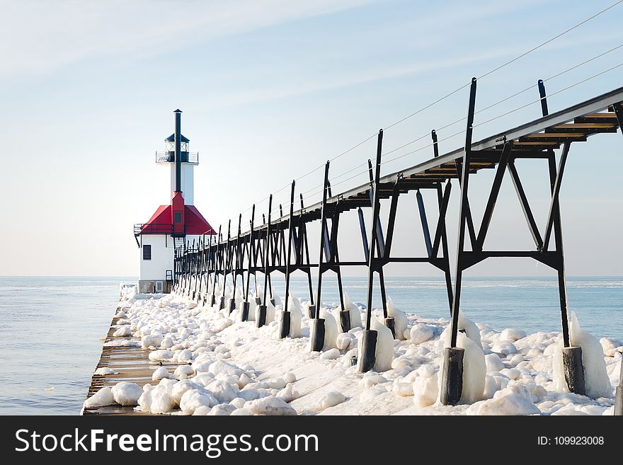 Red and White Concrete Lighthouse Surrounded by Snow Near Body of Water