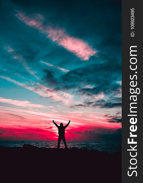 Silhouette of Man Raising Hands Against a Red Sunset Light Under Green Clouds