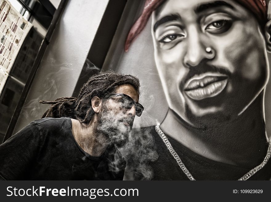 Man With Dreadlocks and Sunglasses Poses Near Tupac Shakur Portrait