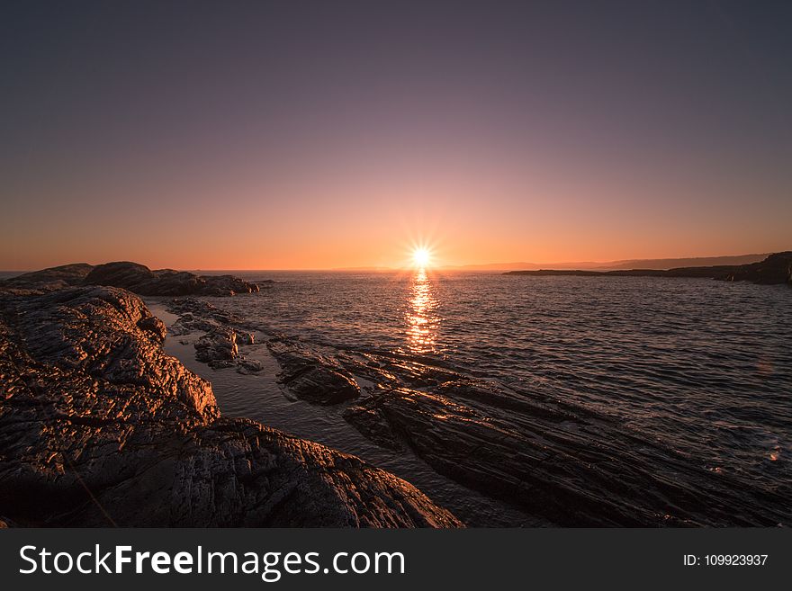 Brown Rocks Beside Body of Water during Sunset