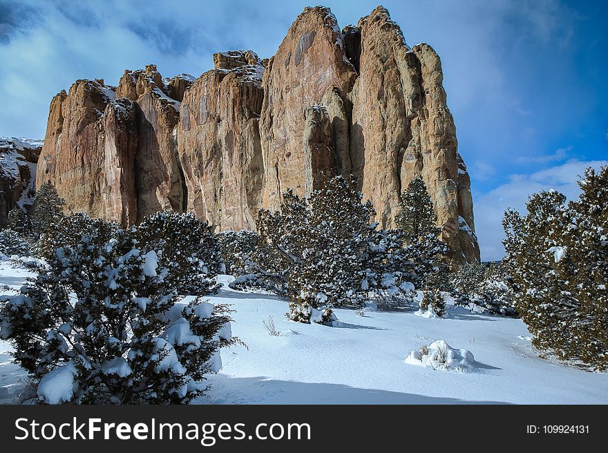 Landscape Photography Of Brown Mountain Near Snowy Trees Under Cloudy Blue Sky