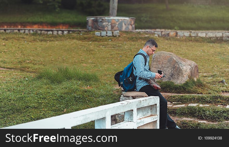 Man Sitting on White Railing Near Rock