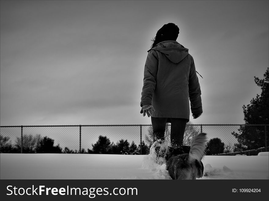 Grayscale Photo Of Person Wearing Coat Walks On Snow