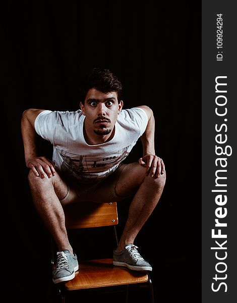 Man Wearing White Crew-neck Short-sleeved Shirt Sitting On Brown Wooden Chair