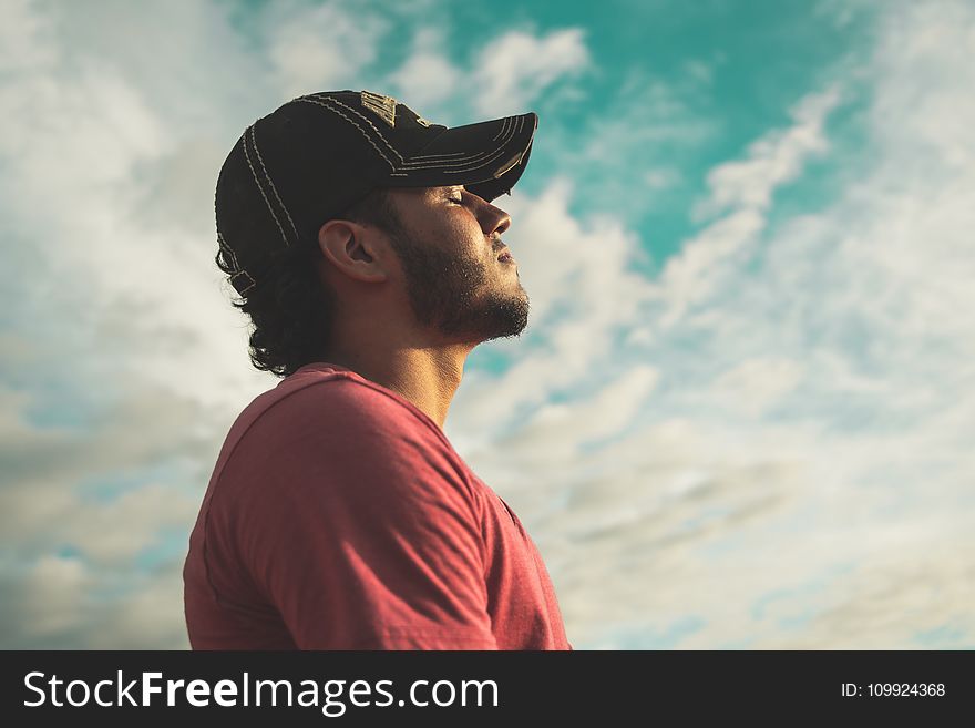 Man Wearing Black Cap With Eyes Closed Under Cloudy Sky