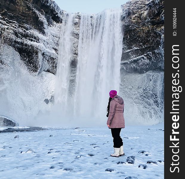 Woman Wearing Pink Snow Coat Standing on Field Full of Snow in Front of Frozen Waterfalls