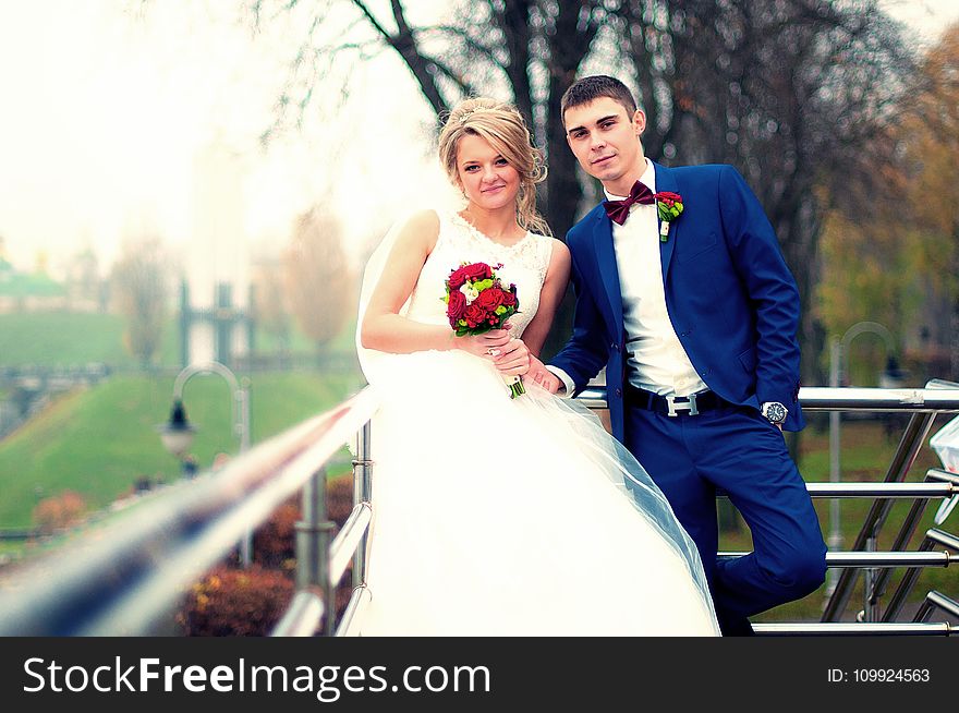 Newly Wed Couple Standing Beside Railing Near Bare Tree