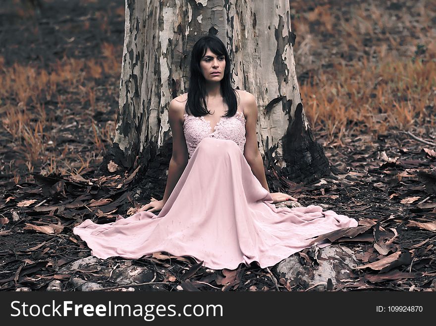 Shallow Focus Photography of Black Haired Woman in Pink Sleeveless Dress Sitting in Front of Tree