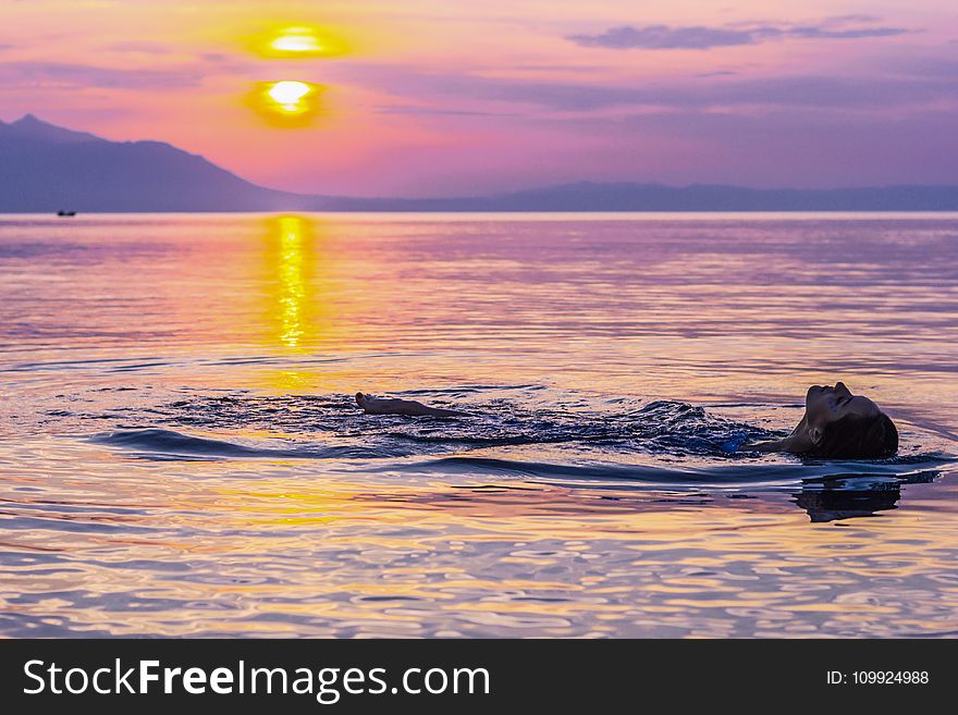 Person Swimming on Body of Water during Golden Hour