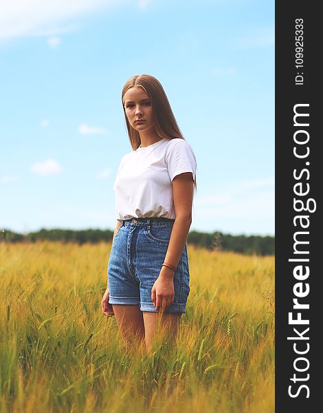 Woman Wearing White Crew-neck T-shirt, Blue Denim Cuff Short Shorts While Standing On Grass Field