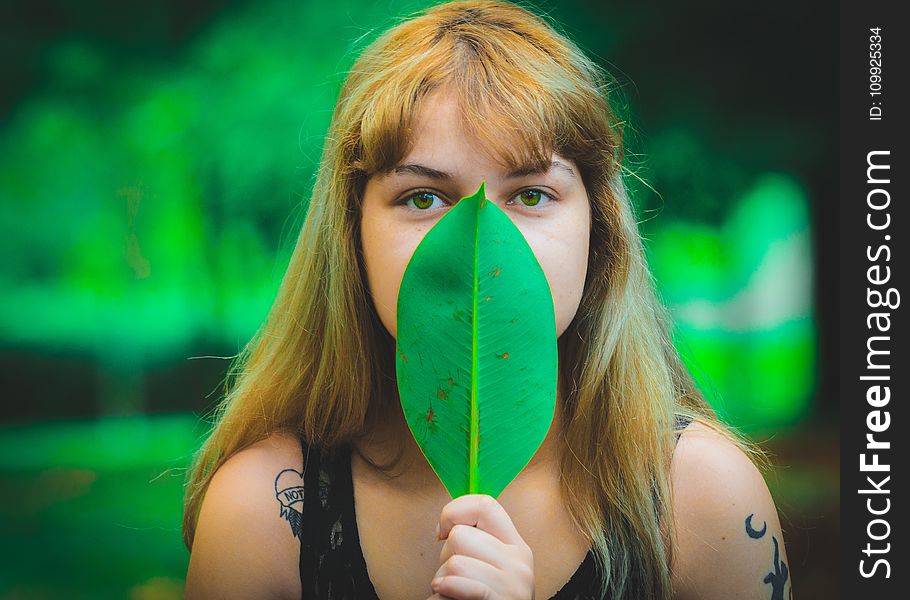 Woman Wearing Black Sleeveless Top Covering Mouth Using Green Leaf