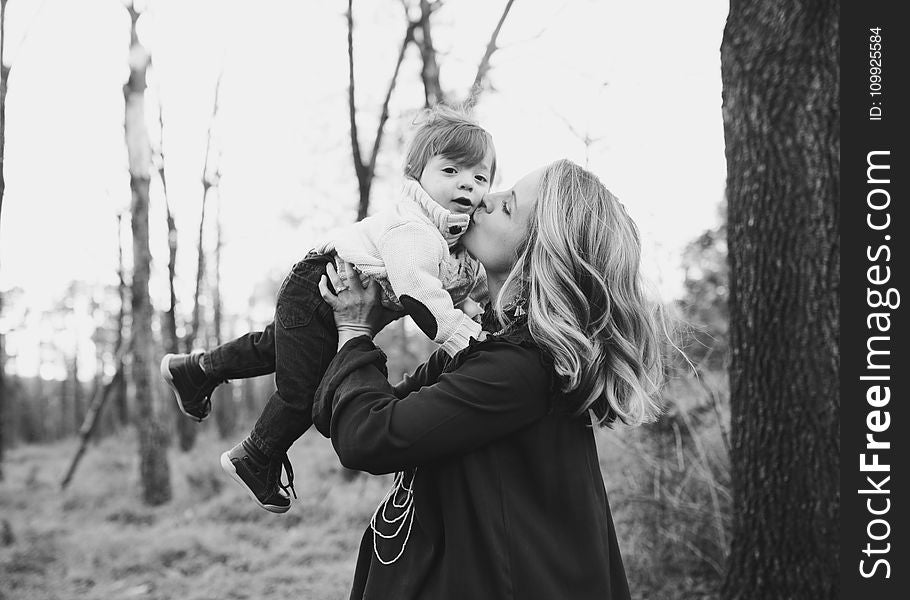 Grayscale Photo Of Woman Kissing Toddler On Cheek