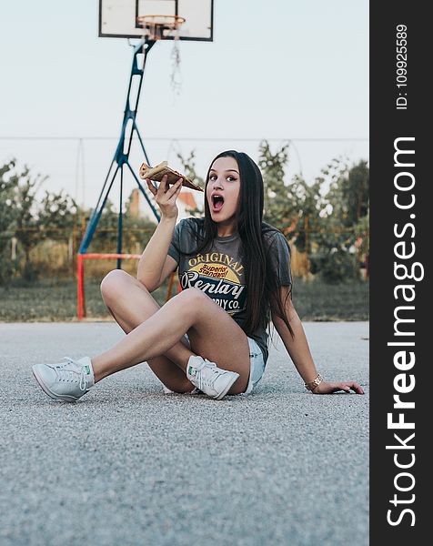 Girl Sitting on Basketball Field Holding Pizza
