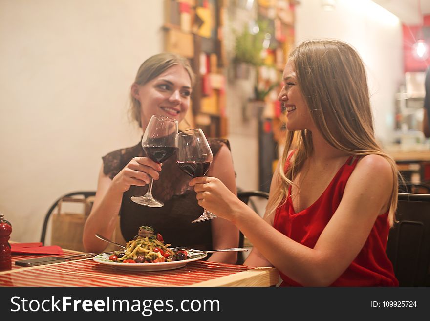 Two Women Holding Long-stem Wine Glasses With Red Liquid