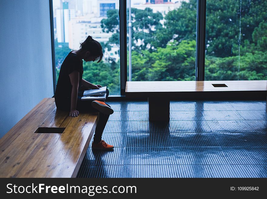 Woman Sitting On Brown Wooden Chair Beside Glass Window