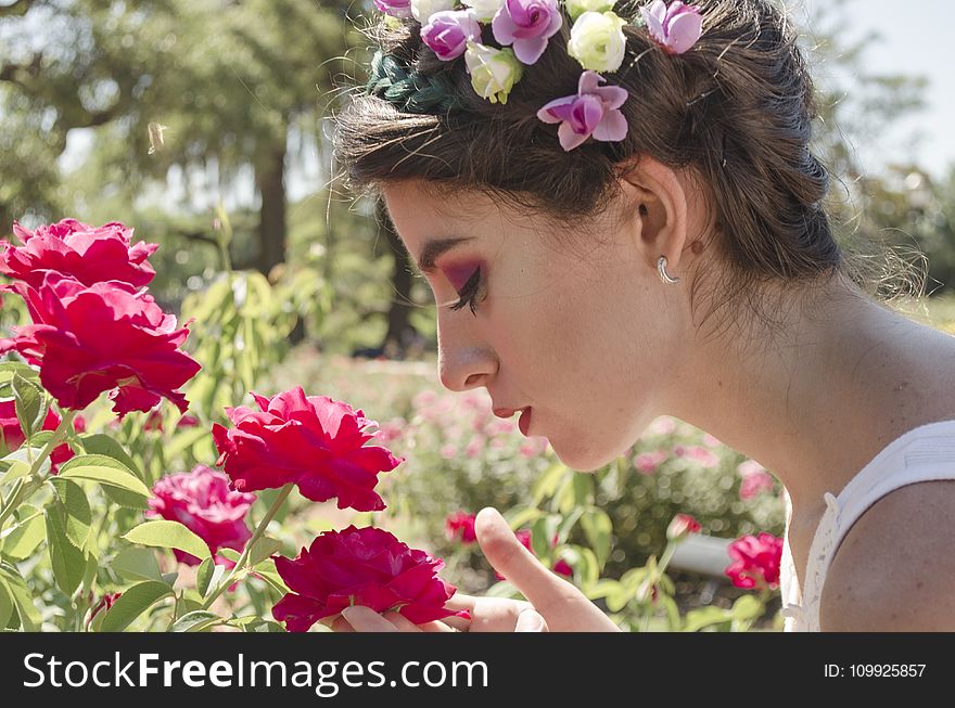 Woman In Floral Headdress Sniffing On Red Flowers