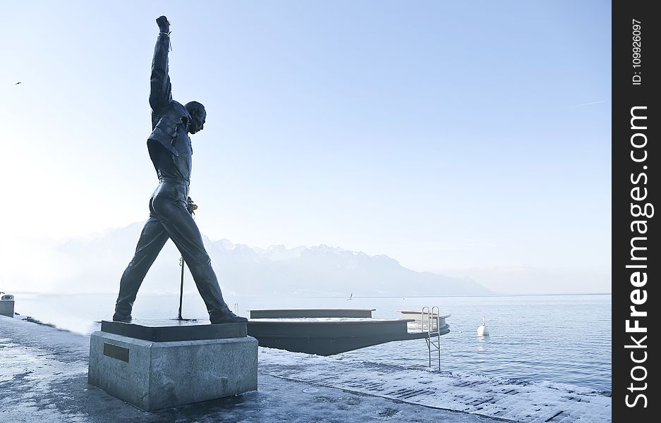 Gray Metal Statue of Man Raising Hand Near Dock