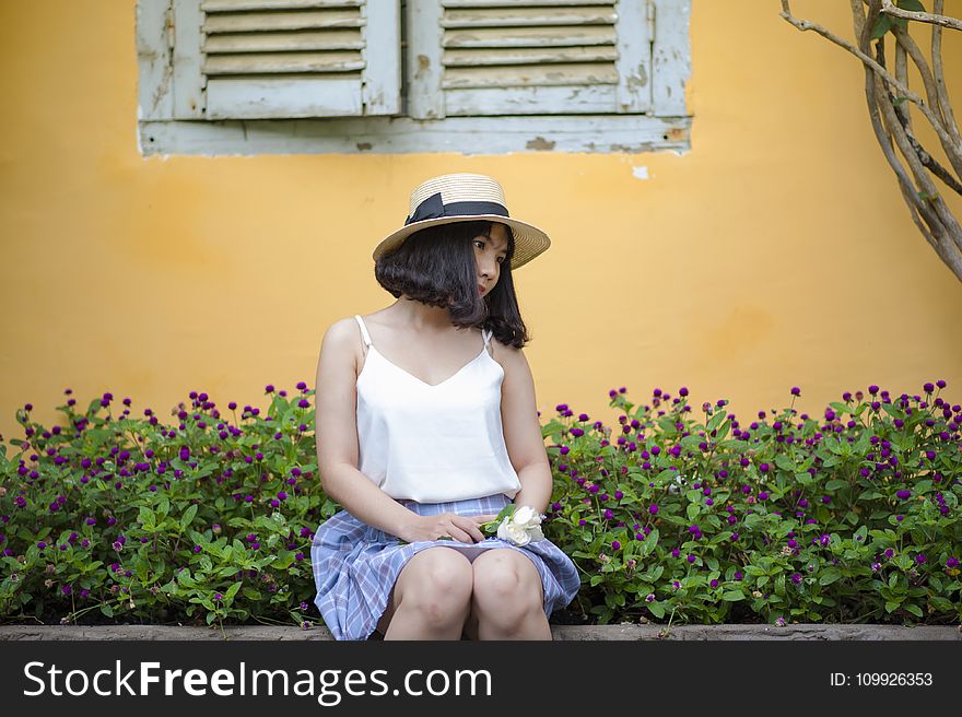 Woman in White Spaghetti Strapped Top With Blue and Purple Plaid Skirt Sitting on Ledge Near Purple Petaled Flower Garden Posing f