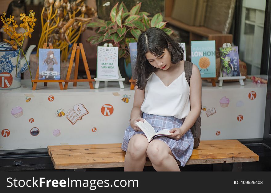 Woman Reading a Book While Sitting on a Bench
