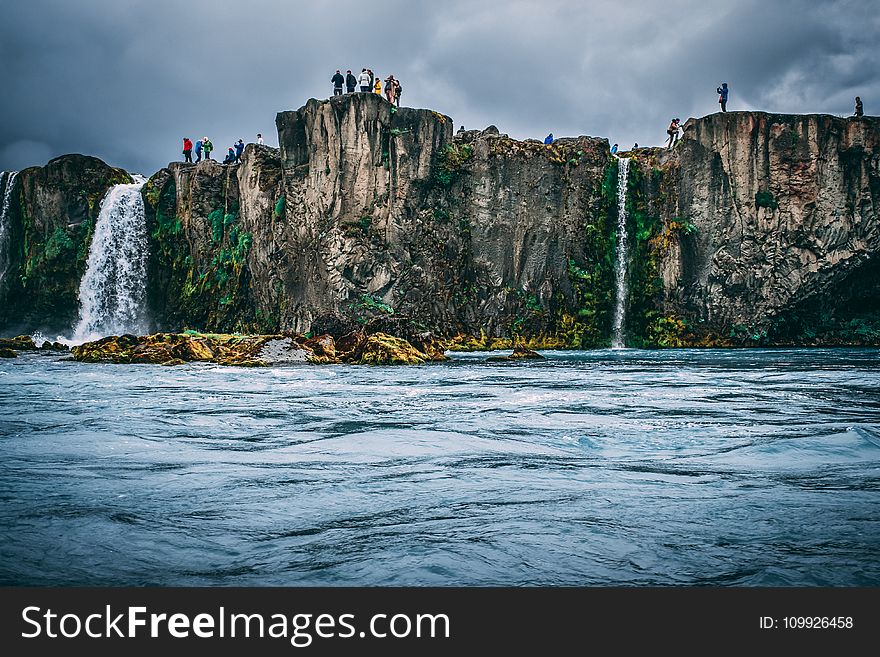 People Near Cliff Under Cloudy Sky