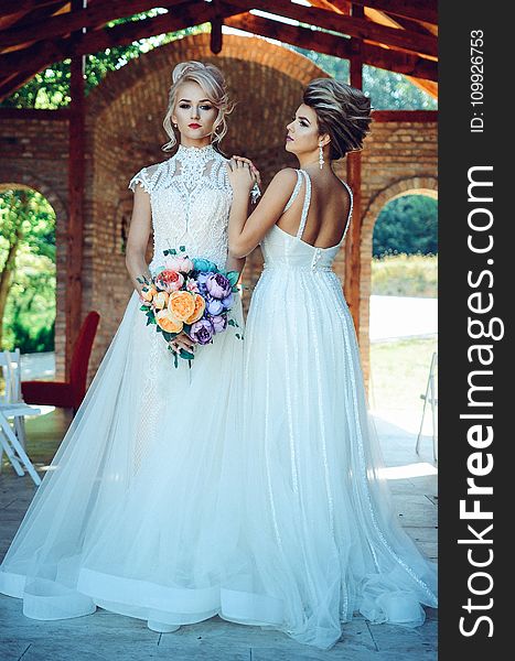 Woman in White Lace Wedding Dress Holding Flower Bouquet Beside Woman in White Dress