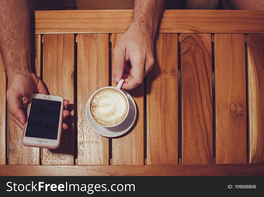 Person Holding Turned Off Gold Iphone 6 With Case And White Ceramic Cup Filled With Latte