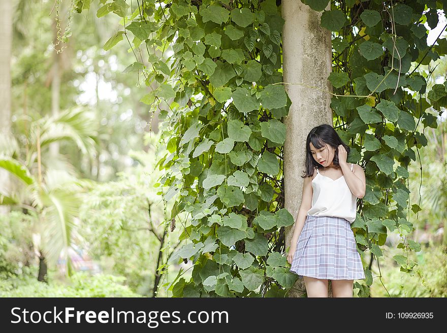 Woman in White Spaghetti Strap Top and Gray Skirt Standing in Front of Tree