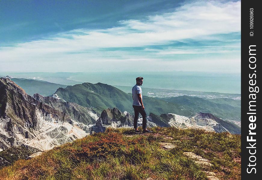 Man Wearing White T-shirt Standing on Mountain Under Blue Cloudy Sky